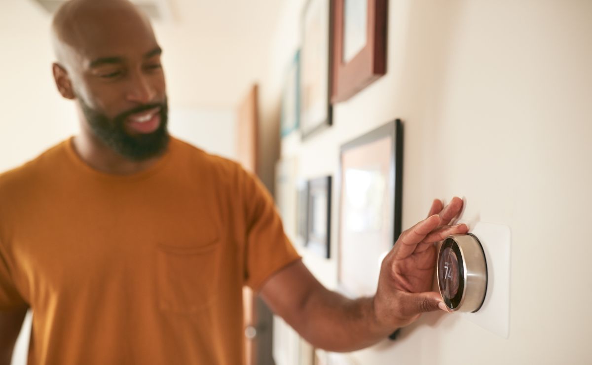 a man in his home checking the temperature and settings on his thermostat